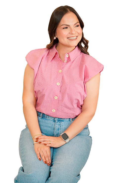 Smiling woman seated, wearing a pink short-sleeve button-up shirt and light-blue jeans.